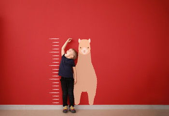 Surprised little boy measuring height near color wall