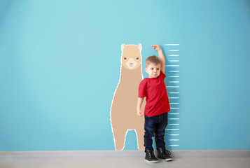Little boy measuring height near color wall