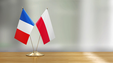 French and Polish flag pair on a desk over defocused background 