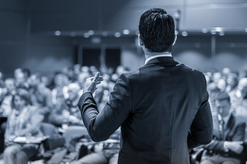 Speaker giving a talk on corporate business conference. Unrecognizable people in audience at...