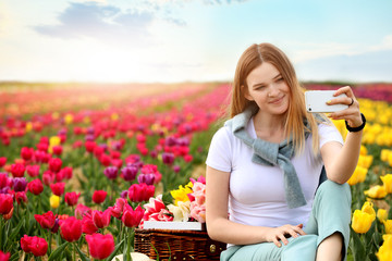 Beautiful young woman taking selfie in tulip field on spring day
