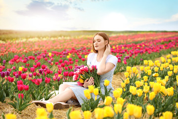Fototapeta na wymiar Beautiful young woman with bouquet of fresh tulips in countryside on spring day