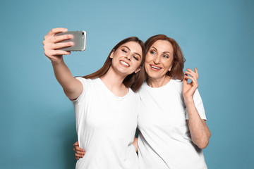 Portrait of happy mother with her daughter taking selfie on color background