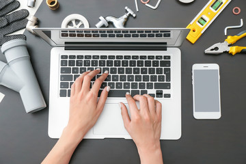 Plumber tools and woman working with laptop on dark background, top view