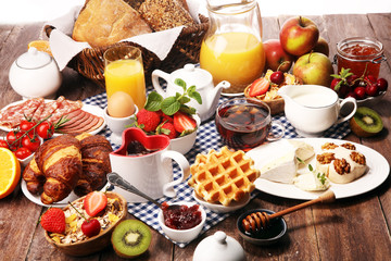 Huge healthy breakfast on table with coffee, orange juice, fruits, waffles and croissants. Good morning concept.