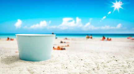 A blue metal bucket with free space for your product. The possibility of mounting bottles with drink, ice cream, food or other products. Blurry beach with people and ocean view. © magdal3na