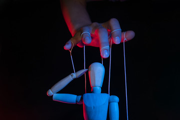 Concept of control. Marionette in human hand. Objects are colored on red and blue light.