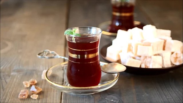 Woman's hand puts turkish tea in traditional glass cup on the wooden table. Oriental.