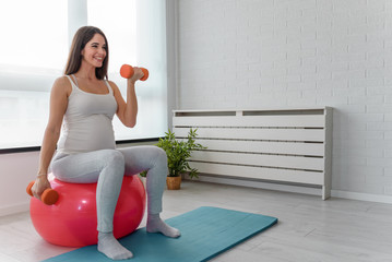 Happy smiling beautiful pregnant woman exercising at home