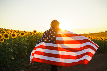Beautiful girl with the American flag in a sunflower field. 4th of July. Fourth of July. Freedom....