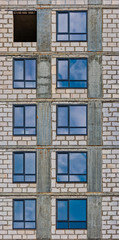 Vertical Row of the windows of apartment building in development state with reflections of blue sky in window glass