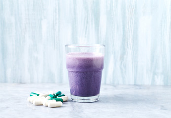 Glass of Protein Shake with milk and blueberries, Beta-alanine and L-Carnitine capsules in background. Sports bodybuilding nutrition. Stone / wooden background.  Copy space.  