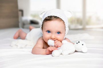 Süßes Baby Mädchen mit Stofftier liegt auf einem Bett und spielt