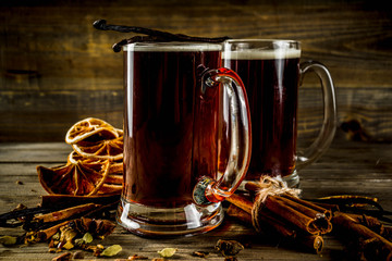 Hot beer with spices - vanilla, cinnamon, anise, citrus. Mulled dark beer drink. Dark wooden background copy space