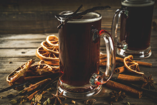 Hot beer with spices - vanilla, cinnamon, anise, citrus. Mulled dark beer drink. Dark wooden background copy space