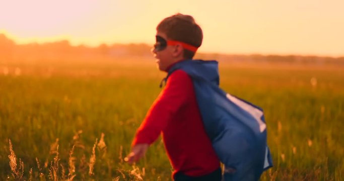 A boy in a superhero costume at sunset runs across the field laughing and smiling