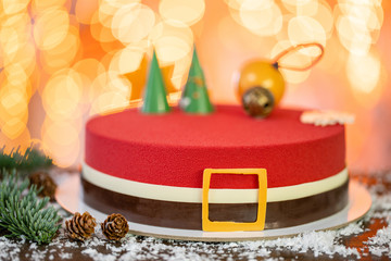 Mini mousse pastry dessert covered with red velour. Garland lamps bokeh on background. Modern european cake. French cuisine. Christmas theme. Copy space