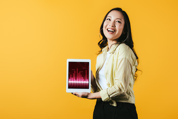 smiling asian girl showing digital tablet with graph, isolated on yellow