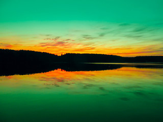 Fototapeta premium Bright colorful sunset over a lake. Beautiful reflection by a tranquil water of amazing sky and the lakeside at sundown in the summer evening. Lake Elovoe (Spruce Lake), South Ural, Russia.