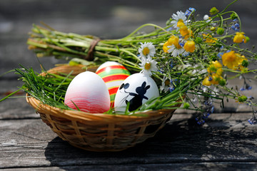 Osterkorb mit bunten Ostereiern, schwarzem gemalten Osterhase, Marienkäfer und bunten Blumen.