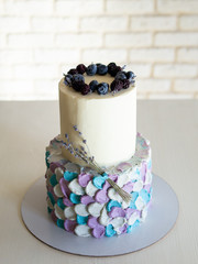 Two-tier cream cake in blue-gray-lilac colors, decorated with blueberries and sprigs of lavender on black stand. Wedding cake, for birthday or anniversary. Selective focus, close up, copy space.