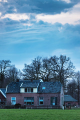 Old farmhouse in dutch countryside with bare trees and cloudy sky.