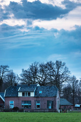 Old farmhouse in dutch countryside with bare trees and cloudy sky.