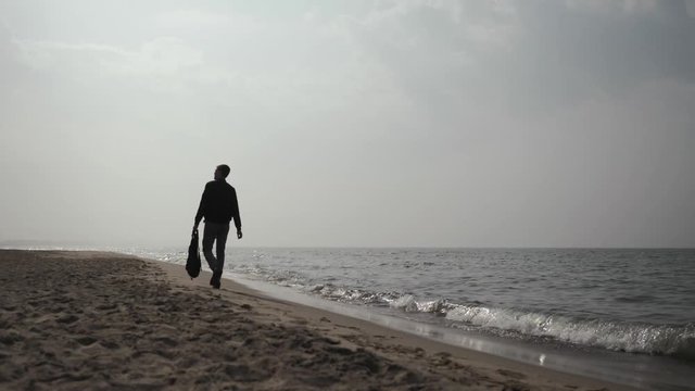 young man 20 years old walks along the coast of the Baltic Sea with a backpack in his hand 