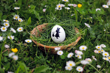 Weidenkorb, Osterkorb mit Osterei, andbemalten schwarzen Osterhasen auf einer Blumenwiese mit Gras und Wildblumen für Kinder