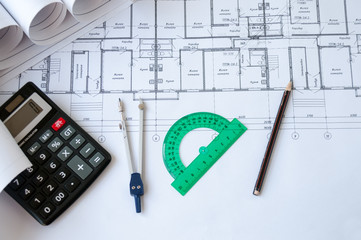 On the table are folded drawings of the apartment, working documentation, compass, protractor, pencil and calculator