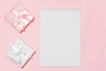 Festive background with gift wrapping with an assortment of boxes of pink silver color with a bow in pastel colors on a delicate pink background with a notebook for writing text with mockup copy space