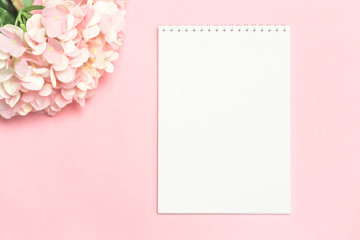 Festive background in pastel colors branch of delicate artificial hydrangea on a pink background with a notebook for writing the text of congratulations with mockup with copy space