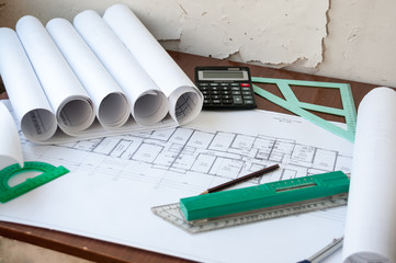 On the table are folded drawings of the apartment, working documentation, compass, protractor,...