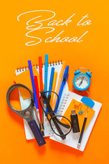 Back to school. Flat lay creative set of school supplies, notebook, pens, markers, alarm clock, compass. School background is orange with the words back to school.
