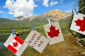 Happy Canada Day. Holiday greeting cards with Maple leaf and Canadian flag. Signs hanging on rope against beautiful Canadian landscape of Canadian Rockies and mountain lakes. People enjoy the holiday