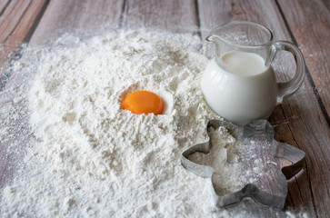 Flour, milk in with a glass jug, orange chicken yolk and a baking dish star on brown wooden table boards