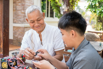 Asian boy and retired grandfather learning building toy house or jigsaw home together at outdoor, making construction from small details. DIY kid, Happy Friendly family members relationship concept.