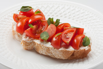 Bruschetta with cherry tomatoes, cream cheese and mint leavs on a white plate