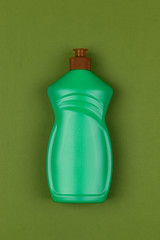 light green plastic bottle of dishwashing liquid on dark green background close-up top view