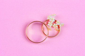 a pair of gold wedding rings and small white flowers in a ring on a pink background, top view flat lay