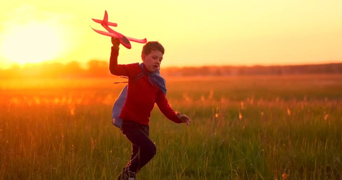 The boy runs across the field with a plane in his hands at sunset