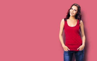 Portrait photo of young smiling woman in casual clothing, blue jeans. Red color background. Copy space.