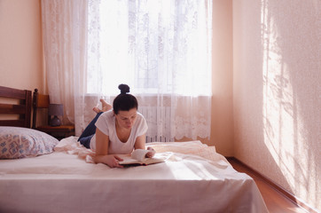 Young woman reading a book on a sunny morning in the cozy bedroom. Education concept.