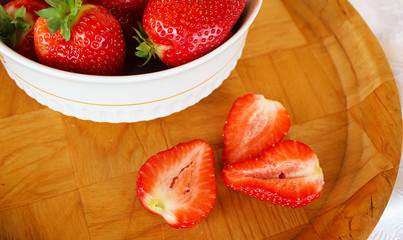 Beautiful cultivated deep red delicious strawberries, macro photography, decoration with fruit in white and wooden plate with peaces