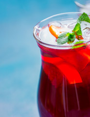 Refreshing non-alcoholic summer detox cleaning beverage. Sangria from variety of fruits orange citrus grape juice karkade iced tea fresh mint in crystal pitcher on blue background