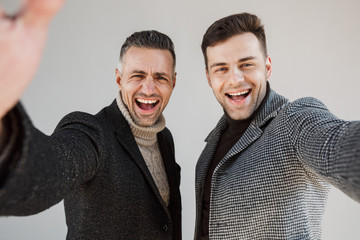 Two handsome men wearing coats over gray background
