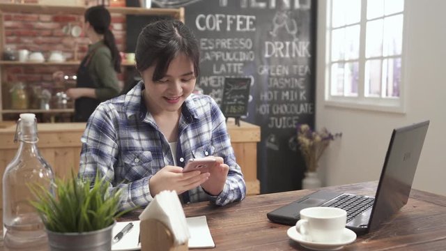Woman typing write message on smart phone in modern cafe bar. young pretty asian girl sitting at table with cup of coffee using mobile phone. female waitress background counter write note order