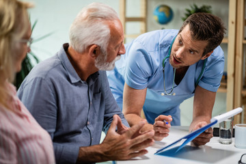 Male doctor analyzing medical documents while talking with senior couple.