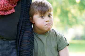 Little boy with down syndrome cuddles up to his mother and looks a bit sad