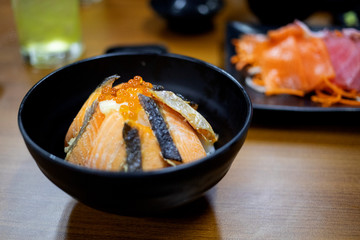 Grilled salmon with eggs topping on rice in black bowl